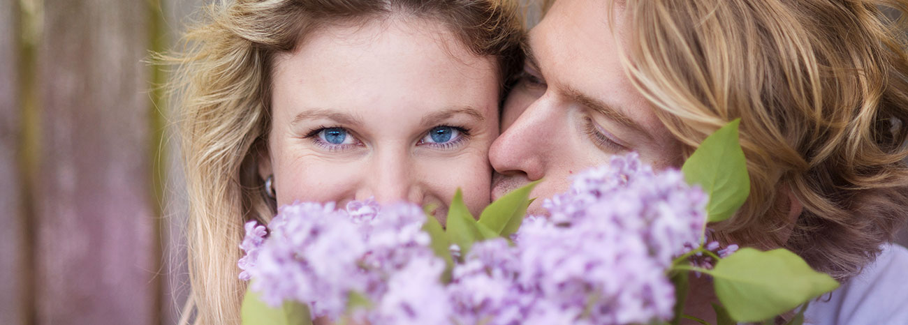Ein Mann küsst seine Freundin, die sich hinter einem Bouquet von lila Blüten versteckt